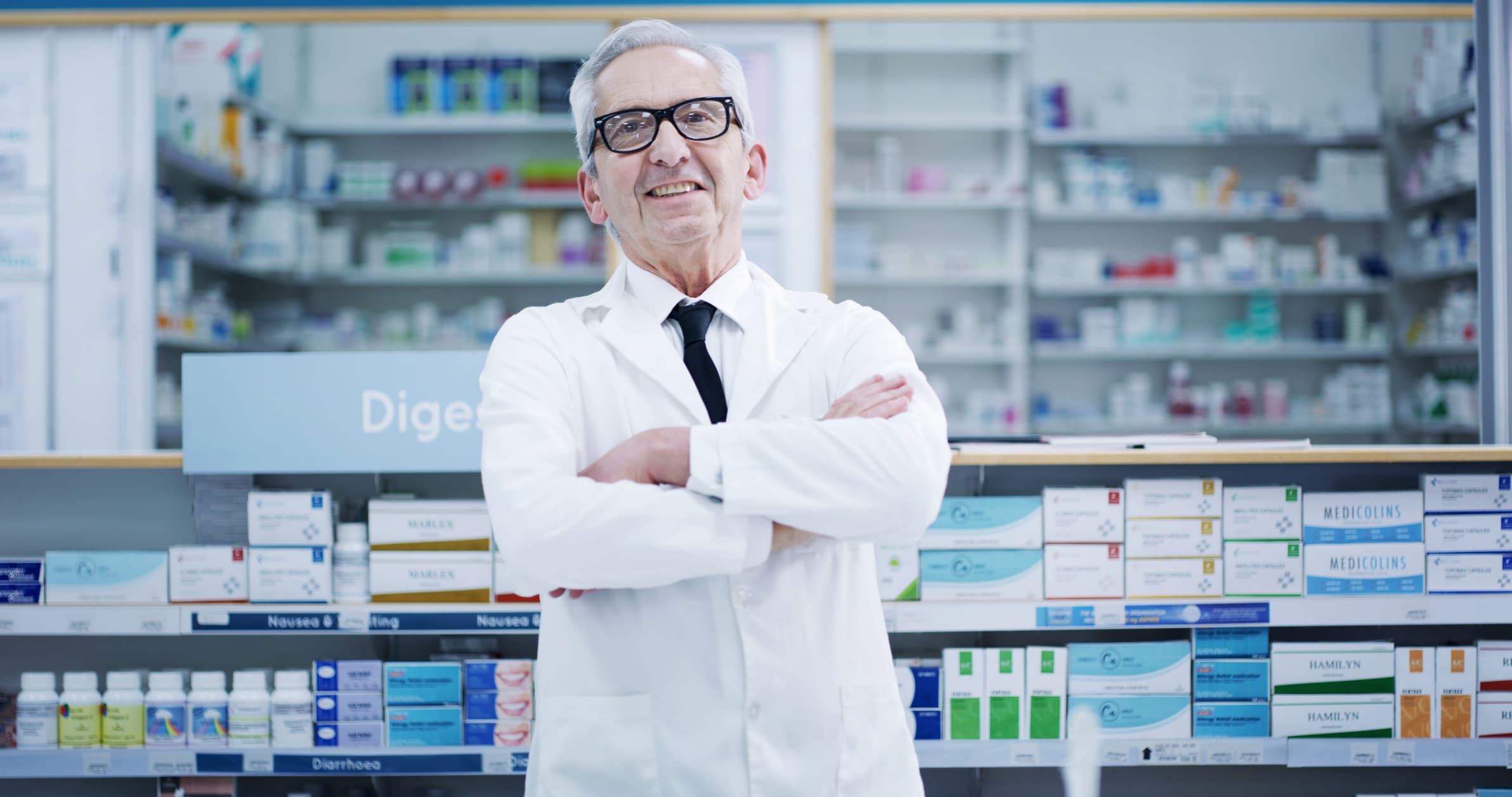 Arms crossed, pharmacy and portrait of mature man in dispensary for cure, treatment or vitamins. Healthcare, medical and supplements with smile of happy pharmacist person in hospital or clinic